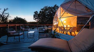 A cozy outdoor seating area with a transparent dome structure, wooden deck, and lounge chairs.