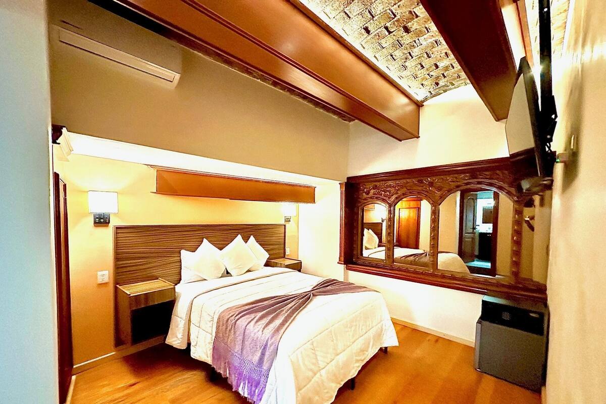 Habitación de hotel con cama de madera, un espejo grande y una lámpara en el techo.