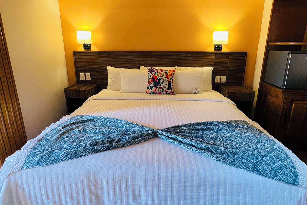 Habitación de hotel con una cama grande, dos lámparas de noche, un refrigerador y techo de ladrillo.