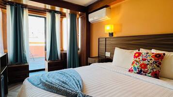 A hotel room with a large bed, a bedside table, a lamp, and a view of the outside.