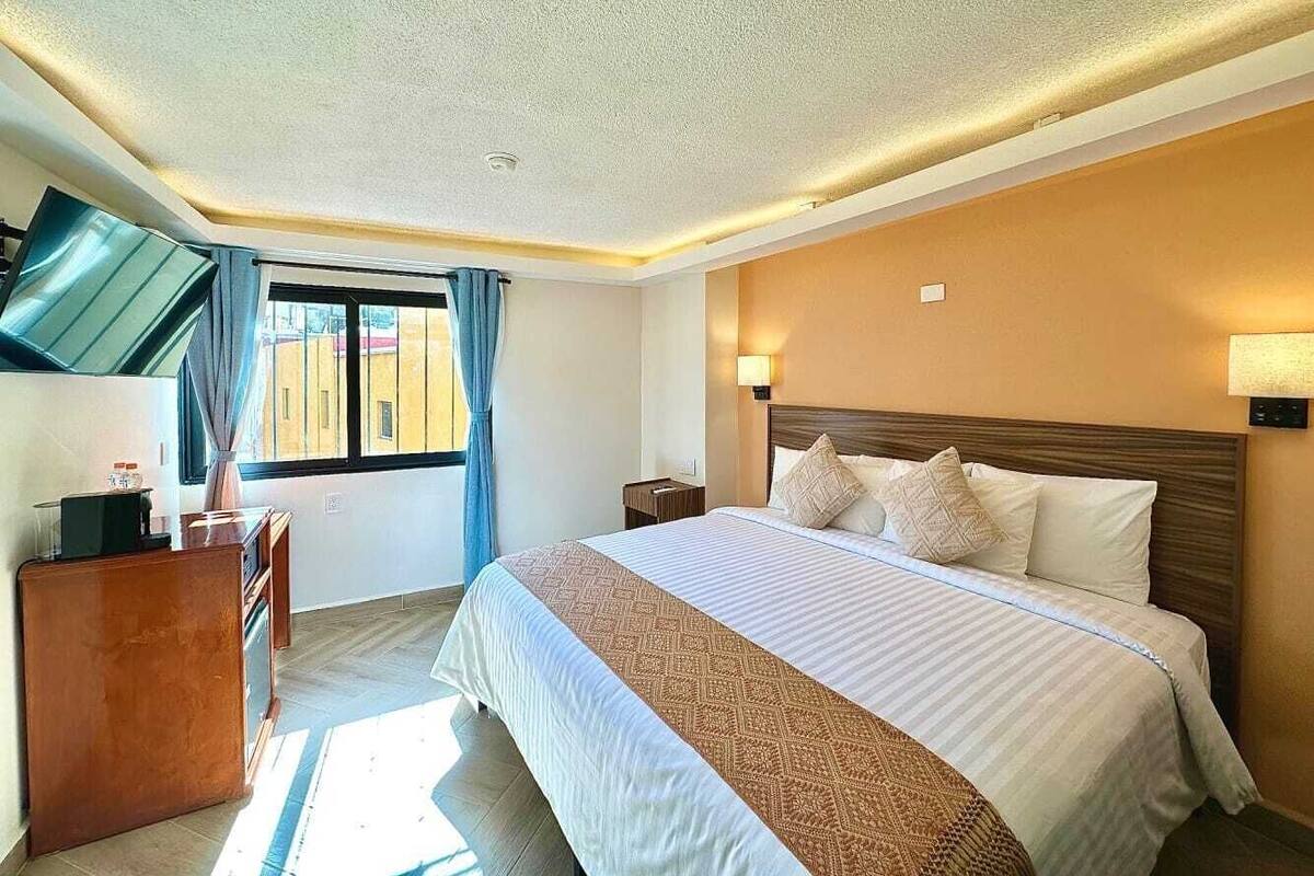 Habitación de hotel con una cama grande, un escritorio, una ventana con cortinas y vistas a edificios.
