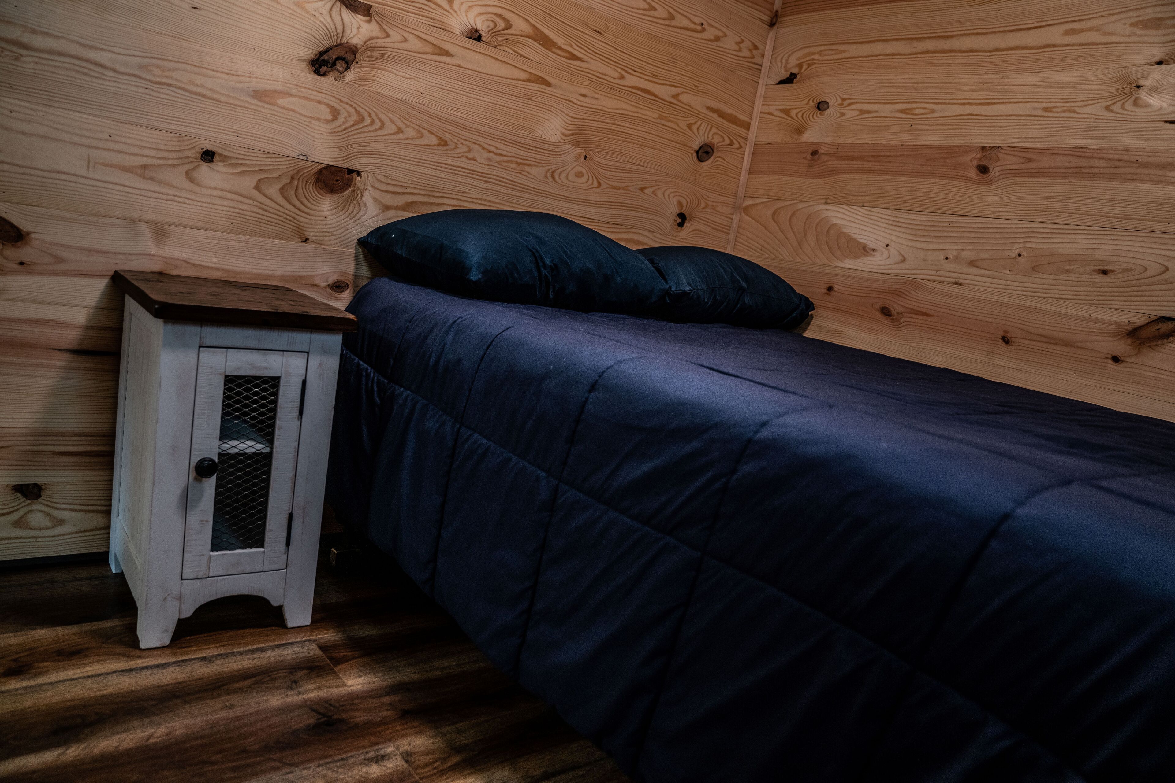 A small wooden room with a single bed, a nightstand, and a small cabinet.