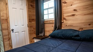 A bedroom with a wooden wall, a white door, a window with curtains, and a bed with blue bedding. - Newly Refurbished 2 Bedroom Duplex cabin in Albany, KY with Slip, Wi-Fi #19 (Albany)