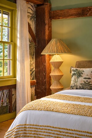 A room with a bed, a lamp, a window with curtains, and a wall with a tropical mural.