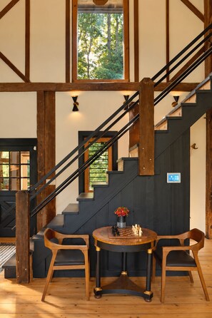 A staircase with wooden beams and black railings, leading to a landing with a table and chairs. - Hudson Retreat - 1780s Renovated Barn (Hudson)