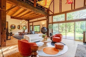 A spacious living room with a high ceiling, large windows, and a fireplace.