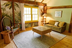 Une pièce chaleureuse avec un plafond en bois, un fauteuil vert, un canapé, un tapis à motifs et une fenêtre avec des rideaux.