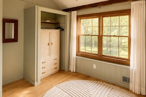 Una habitación con un ventanal grande, suelo de madera y un armario empotrado con cajones.