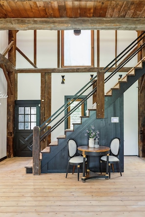 A wooden staircase with a black door at the bottom, a round table with chairs, and a vase with flowers.