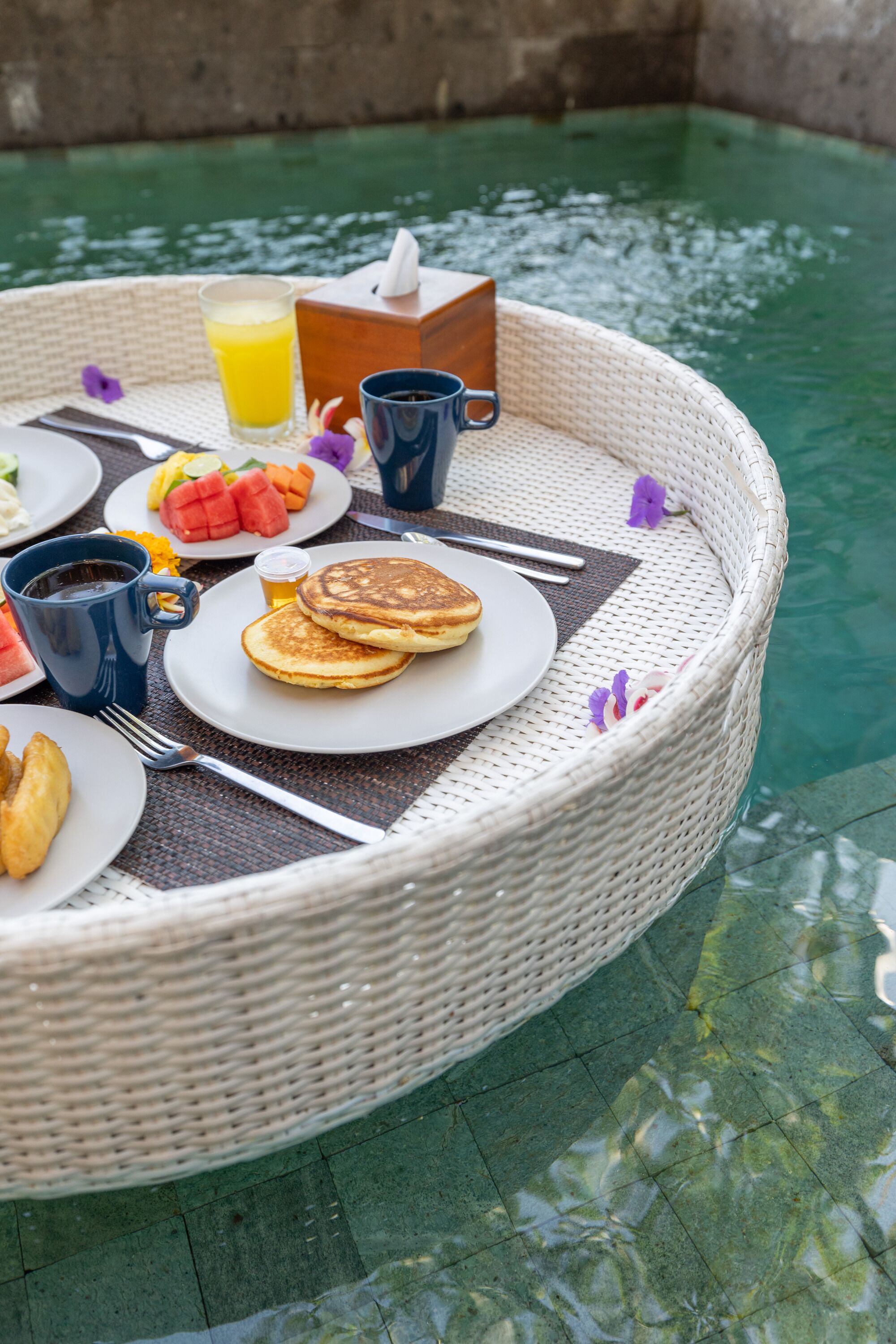 A wicker table with breakfast items including pancakes, a glass of orange juice, and a cup of coffee.