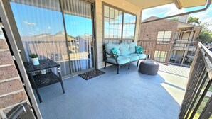 A balcony with a sliding glass door, a sofa with cushions, a small table with a plant, and a round ottoman. - Lake life 1-bedroom,1-bath condo in peaceful Garland TX (Garland)