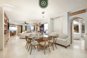 A spacious living area with a dining table, sofas, and a view of the ocean. - Terrasol by Naya Homes (Cabo San Lucas)