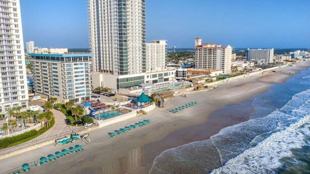 Un hotel frente al mar con edificios altos, una playa y un área de piscina.