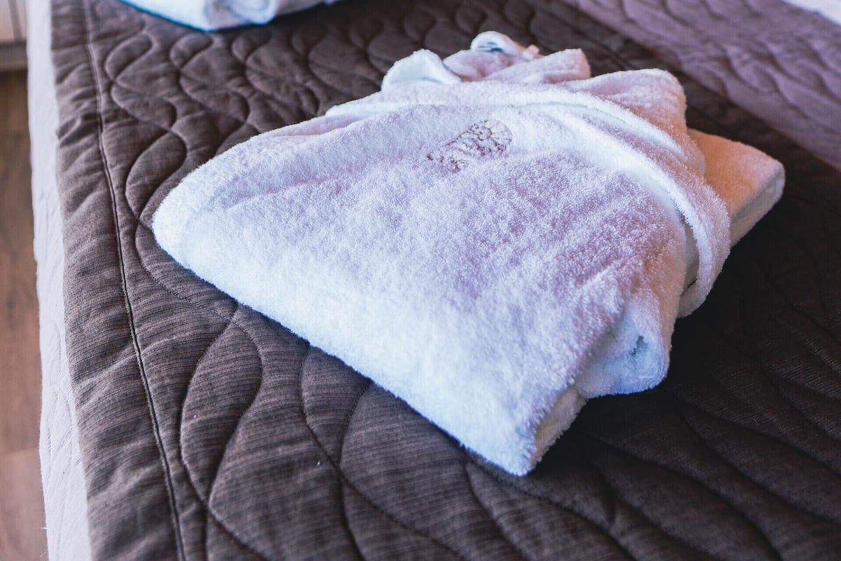 A bed with a quilted mattress and two rolled towels on it.