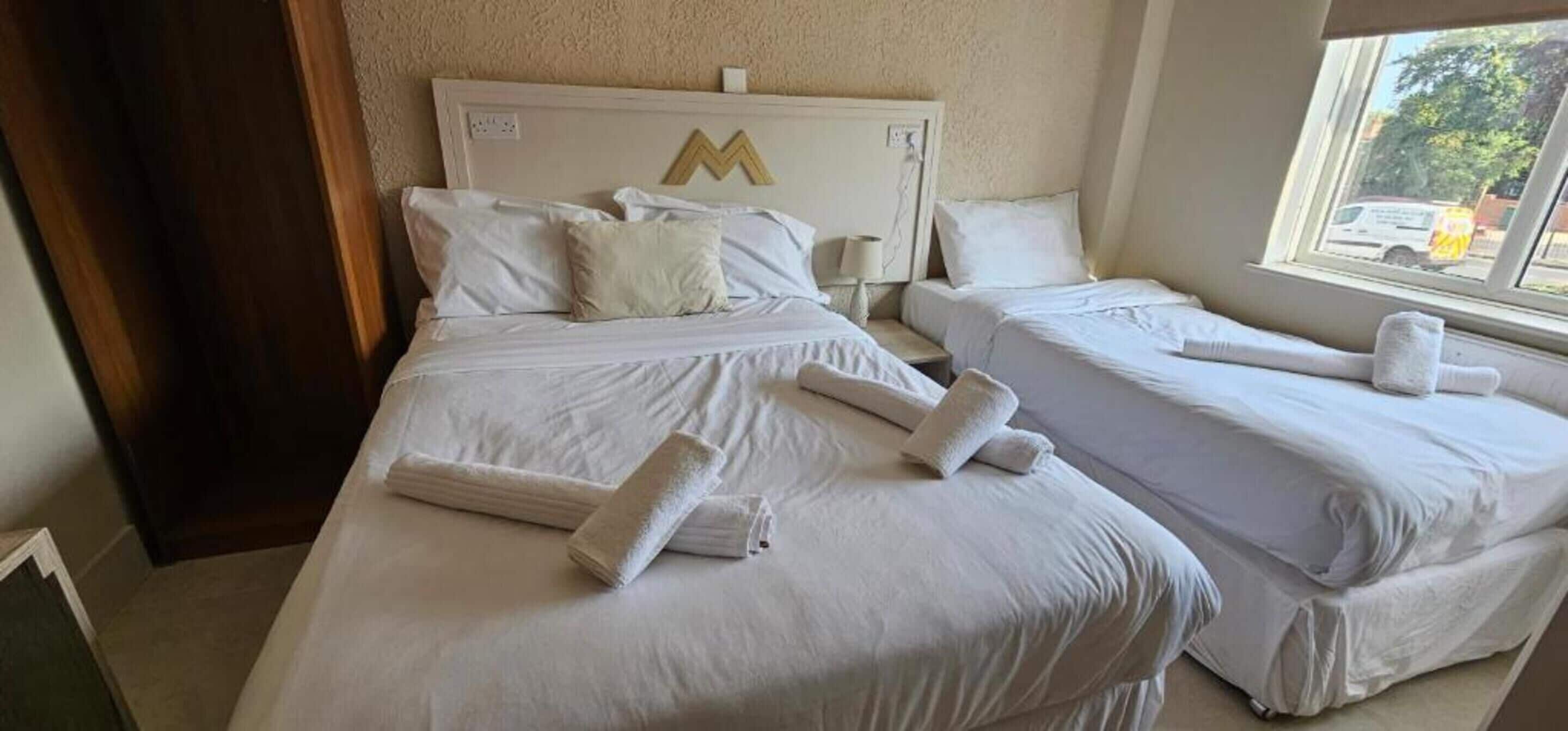 Habitación de hotel con dos camas, cada una con toallas ordenadamente dobladas.