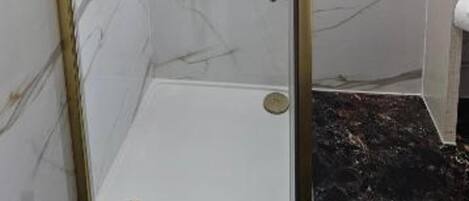 Una ducha con cerramiento de vidrio, marco dorado, paredes de mármol y suelo de mármol negro.