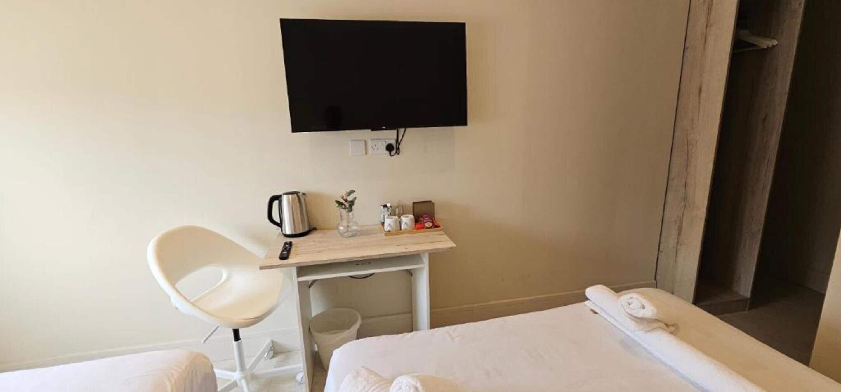 Une chambre d’hôtel équipée d’un lit, d’un bureau avec une bouilloire, d’une chaise et d’un téléviseur fixé au mur.