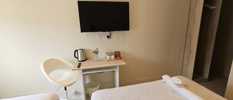 Une chambre d’hôtel équipée d’un lit, d’un bureau avec une bouilloire, d’une chaise et d’un téléviseur fixé au mur.