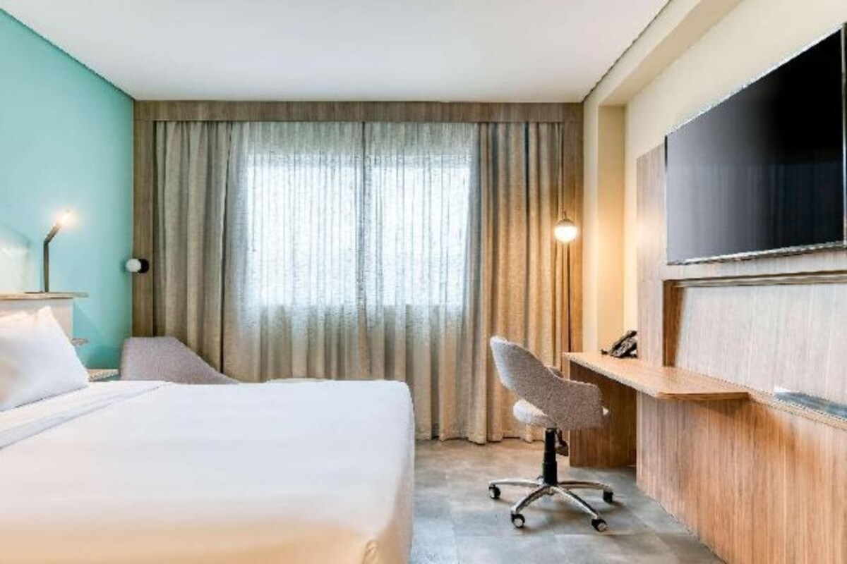 Een hotelkamer met een bed, bureau, stoel, televisie en een raam met gordijnen.