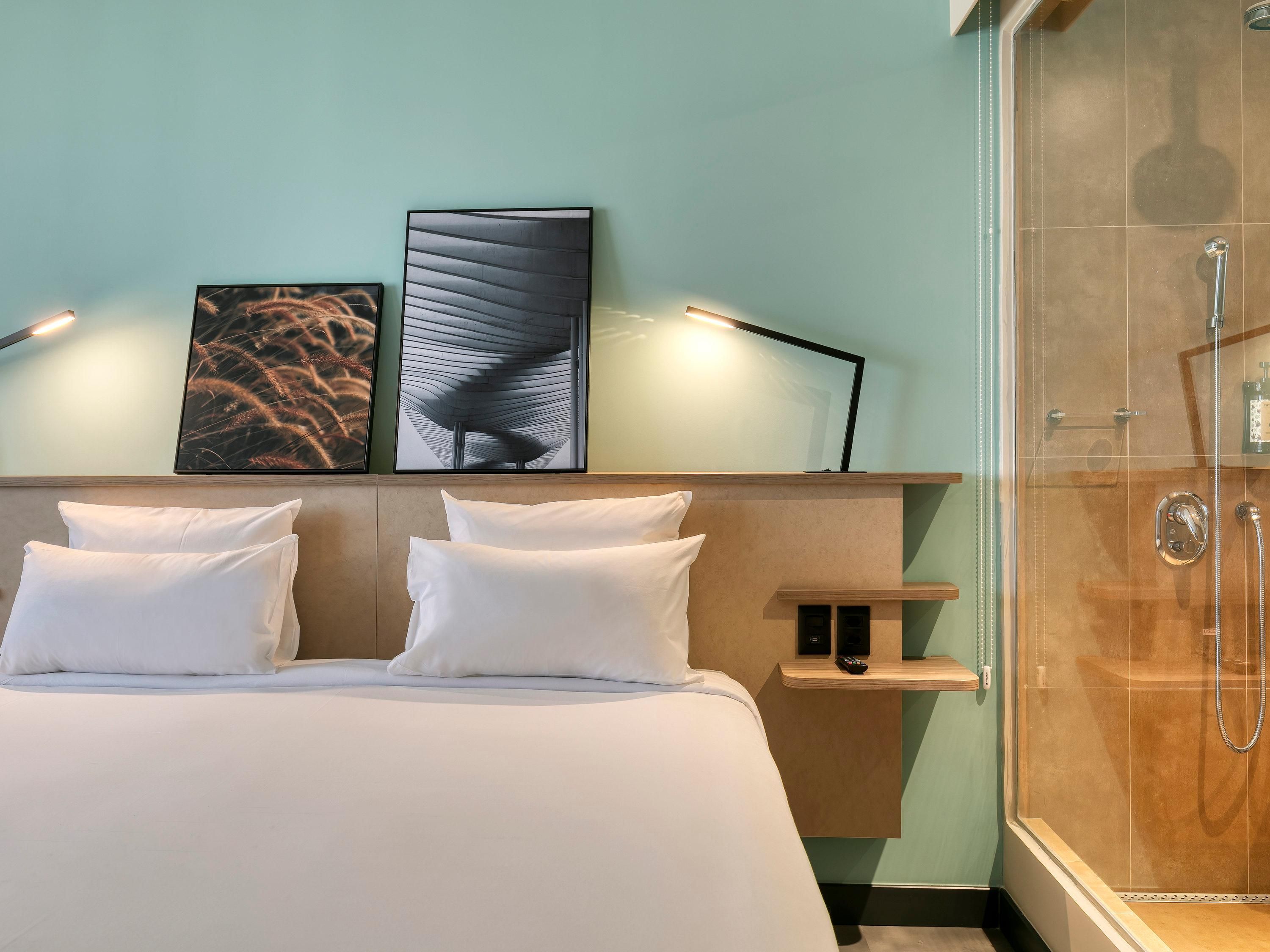 Quarto de hotel com cama, chuveiro e obras de arte na parede.
