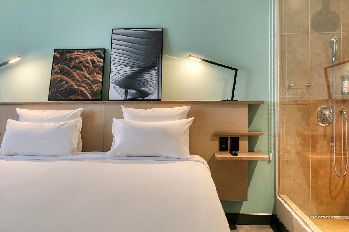 A hotel room with a bed, a shower, and artwork on the wall.