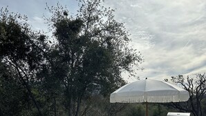 Zona exterior amb taula de pedra i bancs, una barbacoa i un para-sol gran.