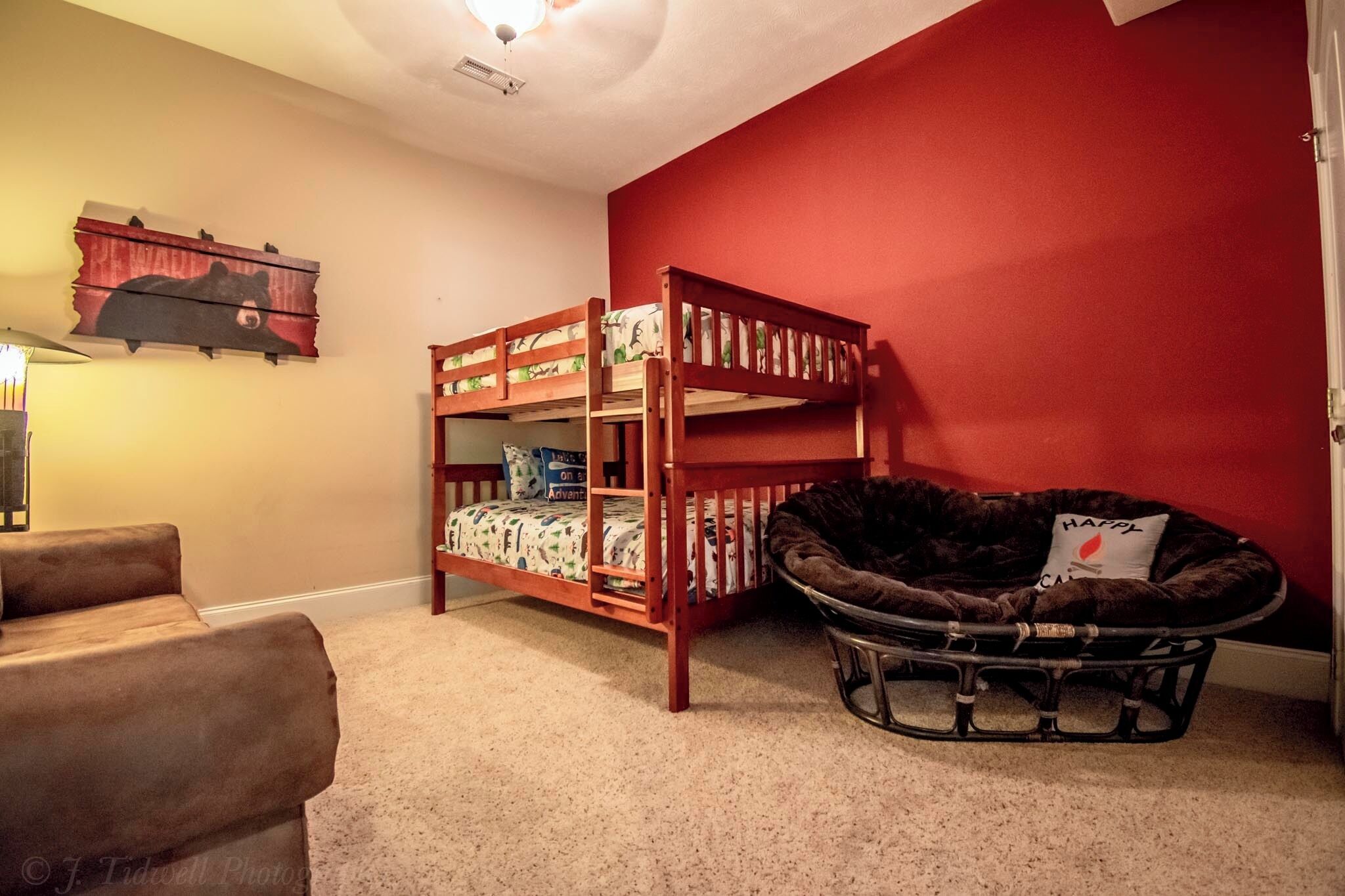 A bunk bed with a cat bed underneath, a couch, and a wall-mounted shelf with a bear picture.