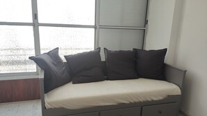 En grå sovesofa med flere puder og opbevaringsskuffer, placeret i et rum med et stort vindue og flisegulv.