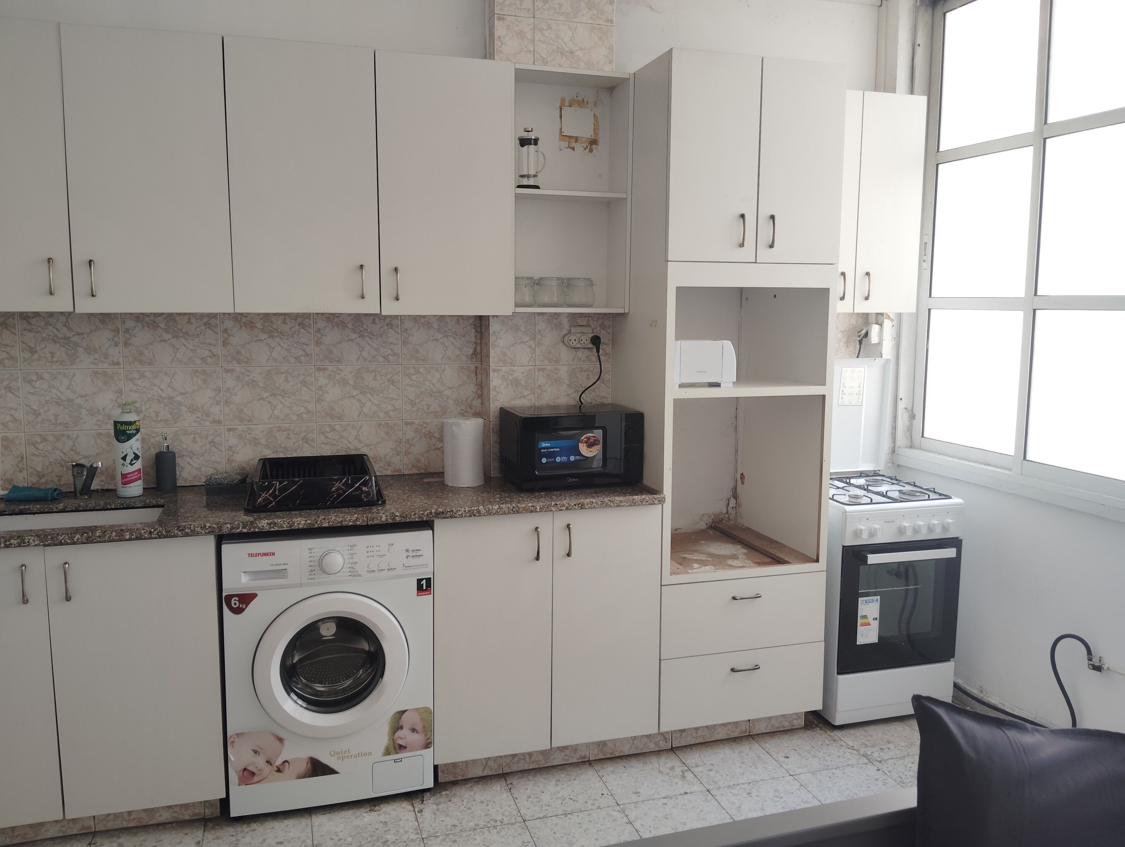 Een kleine keuken met een wasmachine, magnetron en kookplaat.