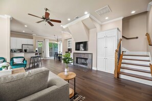 A spacious living area with a fireplace, a kitchen in the background, and a staircase with wooden railings. - 1 mi to AT&T / King Beds / Game-room / Study Desks (Arlington)