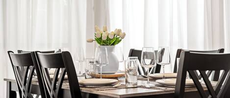 A dining table set with white plates, clear glasses, and a vase of white tulips.