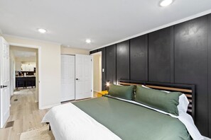 Une chambre à coucher comprenant un lit, une table de chevet, une commode, une armoire et une porte donnant sur une salle de bain.