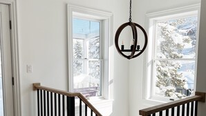 A staircase with black railings and wooden steps, leading to a room with white walls and large windows. - Charming Cottage steps to restaurants, shops & slopes (Park City)