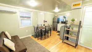 Un espace de vie compact comprenant un coin repas, une kitchenette et un canapé avec des coussins.