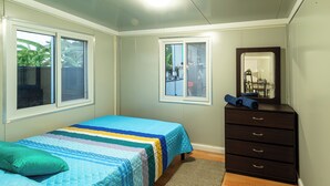 Une chambre à coucher avec un lit, une commode, un miroir et des fenêtres.