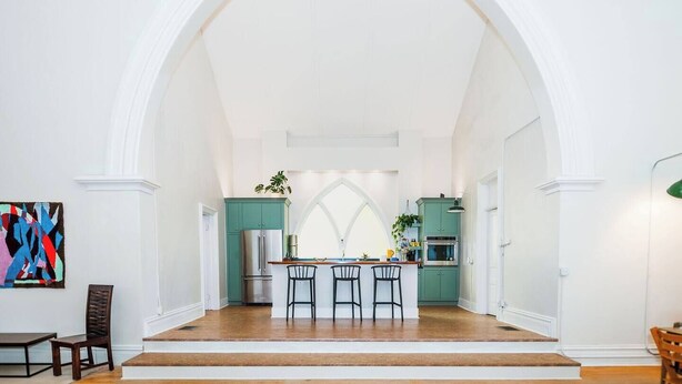 A spacious kitchen with a central island, a dining area with chairs, and a large arched doorway leading to another room. - Find Your Sanctuary at The Church (Helena)
