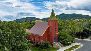 A red brick church with a green steeple, surrounded by trees and hills. - Find Your Sanctuary at The Church (Helena)