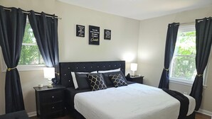 Une chambre à coucher avec un grand lit, des rideaux sombres, une table de chevet avec une lampe et trois citations inspirantes affichées sur les murs.