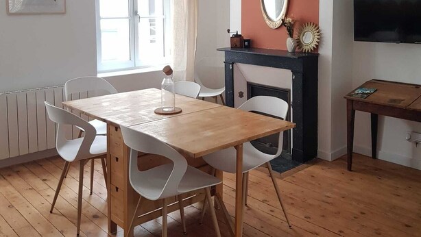 A dining area with a wooden table and white chairs, a fireplace, a television, and a window with curtains. - La Sirène, Entre le zoo de Beauval et les Châteaux de la Loire (Romorantin-Lanthenay)