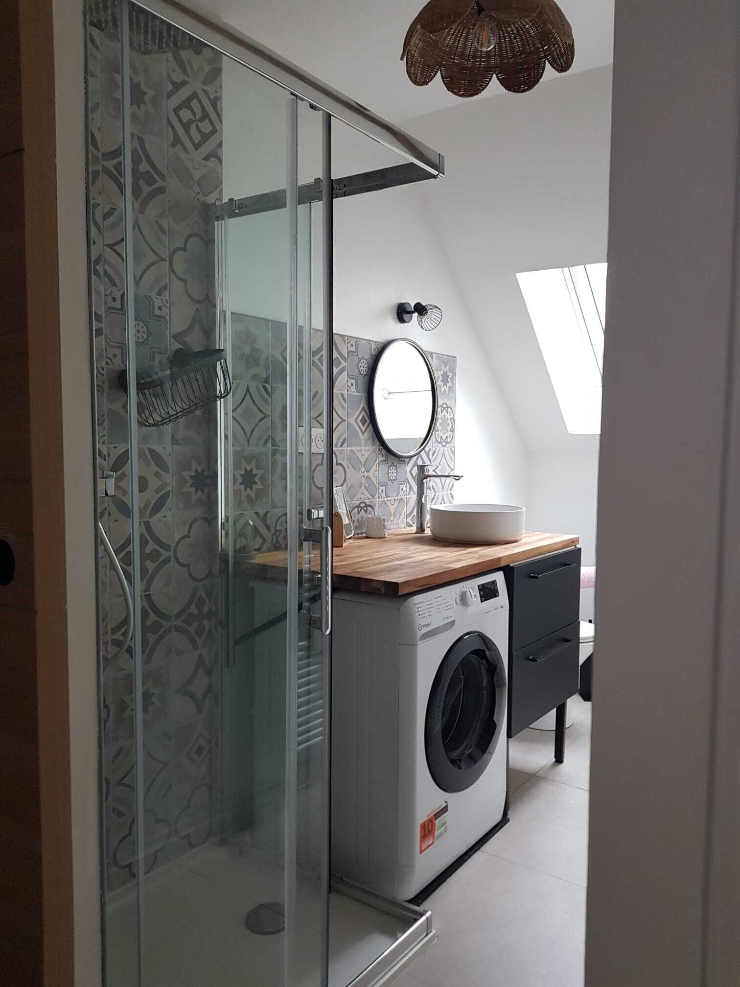 A modern bathroom with a glass shower enclosure, a washing machine, and a wooden countertop with a sink.