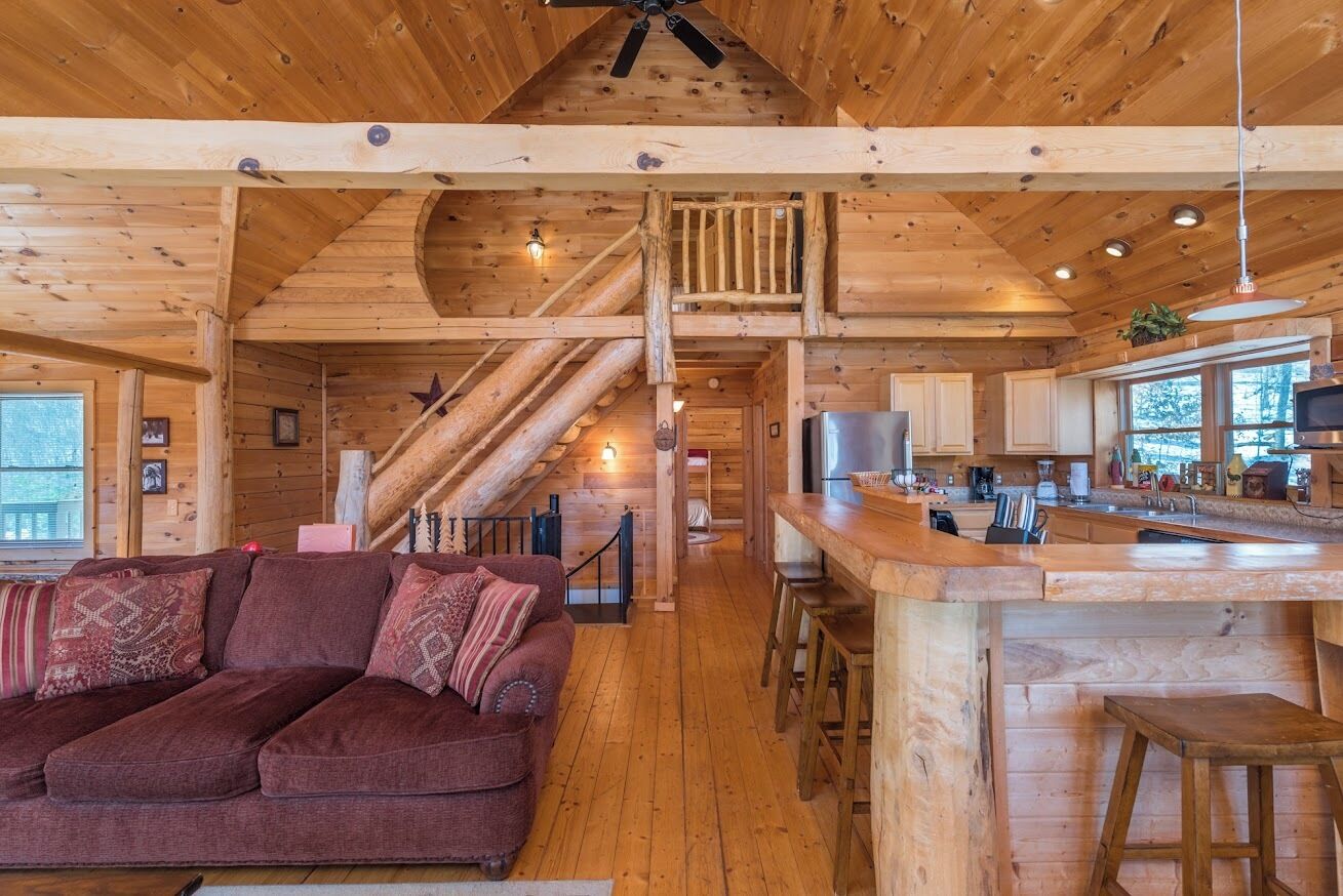 A cozy cabin interior with a wooden staircase, a living area with a sofa, and a kitchen area with a bar.