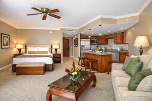 A hotel room with a bed, a sitting area with a couch and a coffee table, a kitchenette, and a ceiling fan.