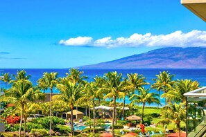 A resort with a pool, palm trees, and a view of the ocean and a mountain.