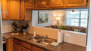 A kitchen with wooden cabinets, a granite countertop, a double sink, and a window with a view of a living area. - Waterfront Getaway and BBQ (Hudson)