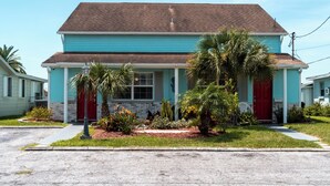 A two-story house with a red door, a front porch, and a small garden with palm trees and cacti. - Waterfront Getaway and BBQ (Hudson)