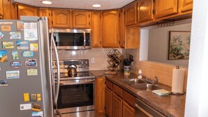 A kitchen with wooden cabinets, stainless steel appliances, a refrigerator, a microwave, an oven, a sink, and a dish rack. - Waterfront Getaway and BBQ (Hudson)