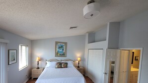 A bedroom with a bed, nightstands, a painting, a door, and a view into another room. - Waterfront Getaway and BBQ (Hudson)