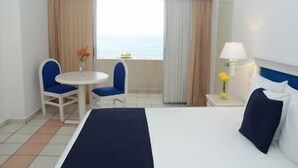 Une chambre d’hôtel avec un lit, deux chaises, une petite table, une lampe et une fenêtre avec des rideaux.