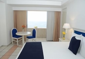 A hotel room with a bed, two chairs, a small table, a lamp, and a window with curtains. - Sunset Palace Beach Hotel - All Inclusive (Mazatlán)