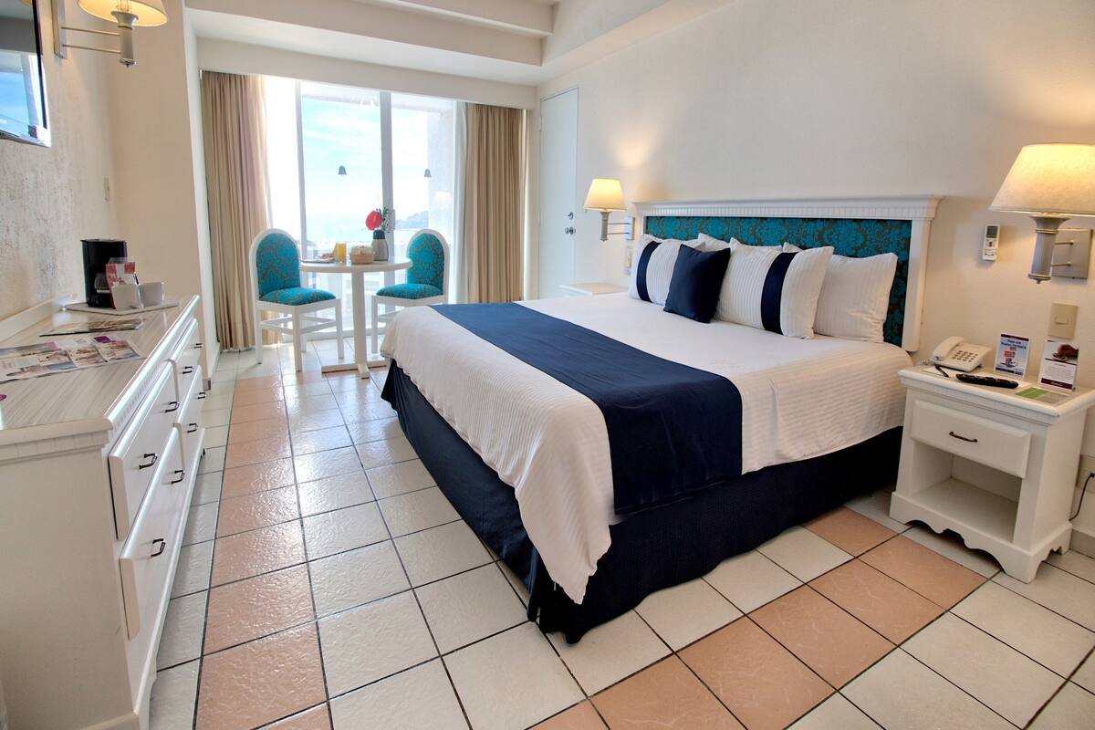 Habitación de hotel con cama, escritorio, silla, mesa y vistas al exterior.